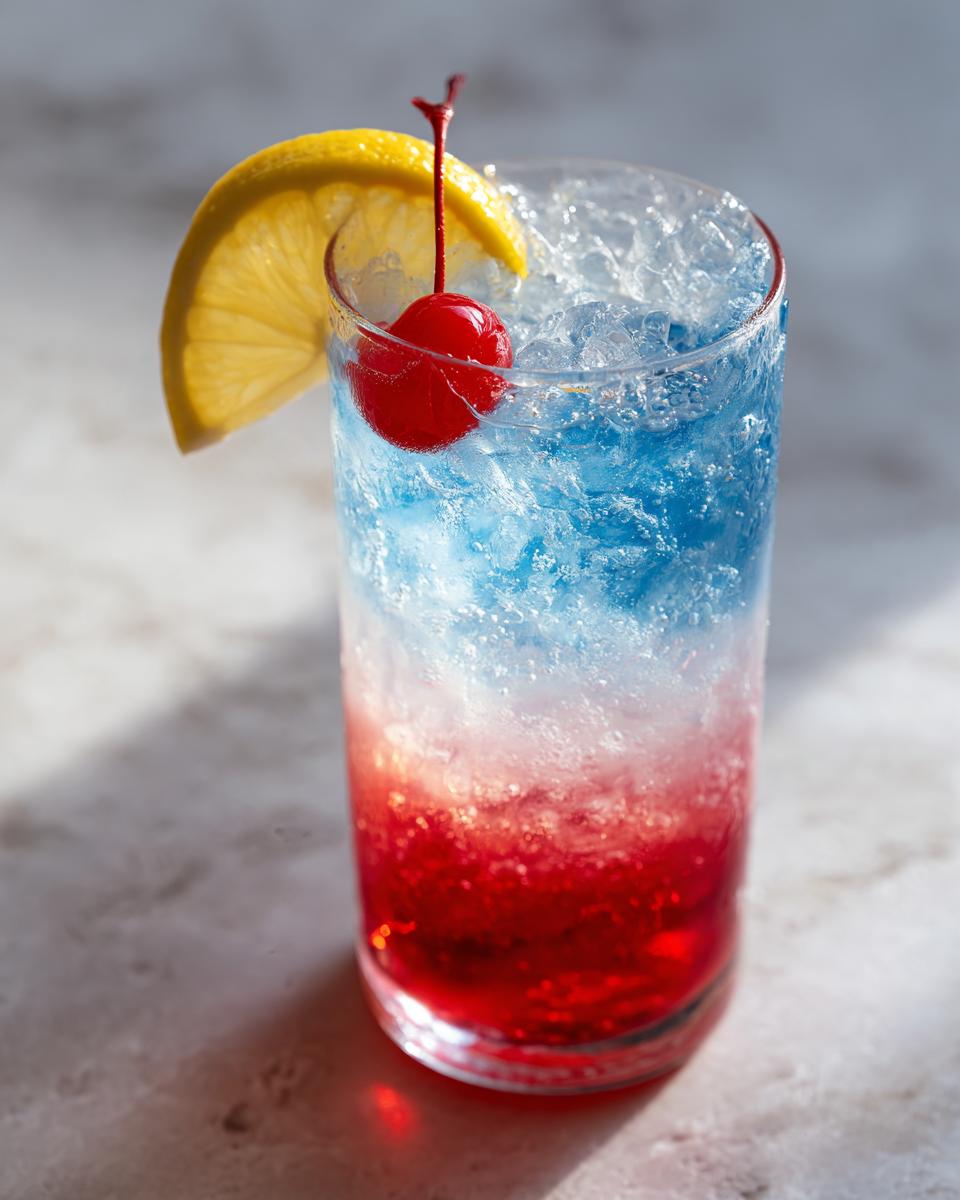 Patriotic Layered Lemonade: Joyful Holiday Drink 4 A tall glass filled with a Patriotic Layered Lemonade Refreshing Holiday Drink, featuring red, white, and blue layers, garnished with a lemon slice and cherry.