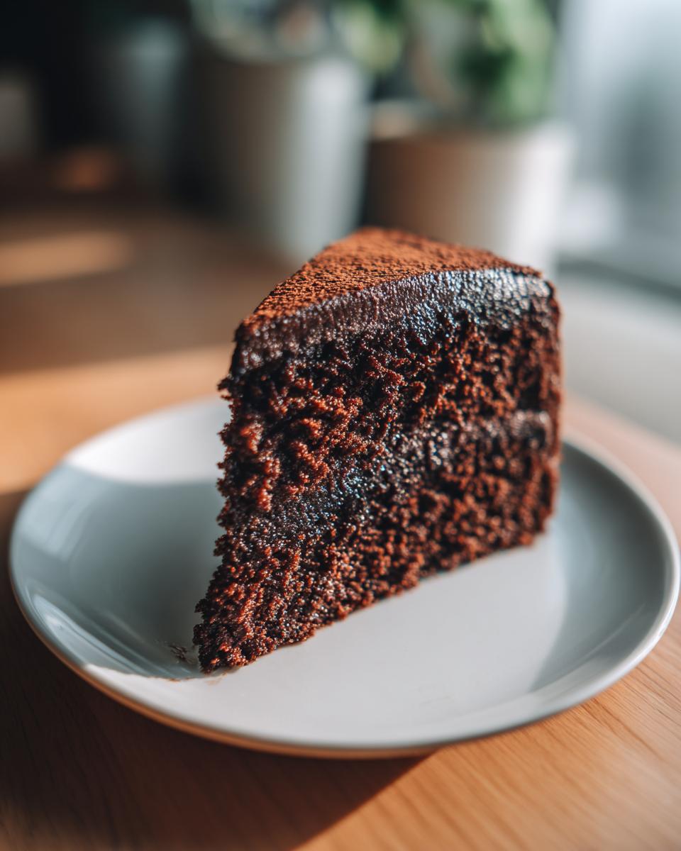 Decadent Chocolate Birthday Cake: Pure Bliss 5 A moist slice of decadent chocolate birthday cake dusted with cocoa powder on a white plate.