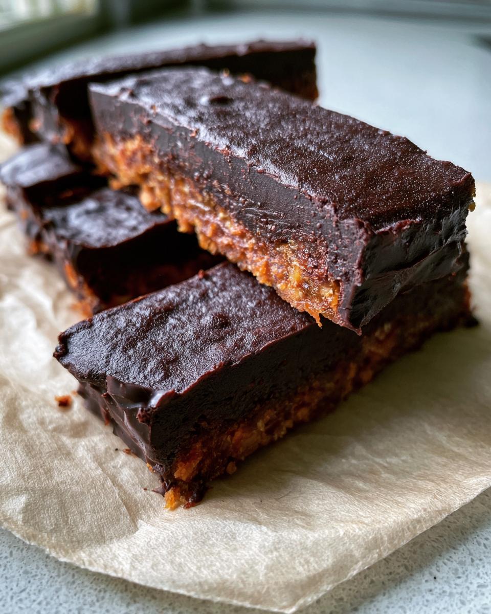 Healthy Date Snickers That Beat Your Sugar Cravings 4 Close-up of stacked Healthy Date Snickers bars with a rich chocolate topping and a date-nut base.
