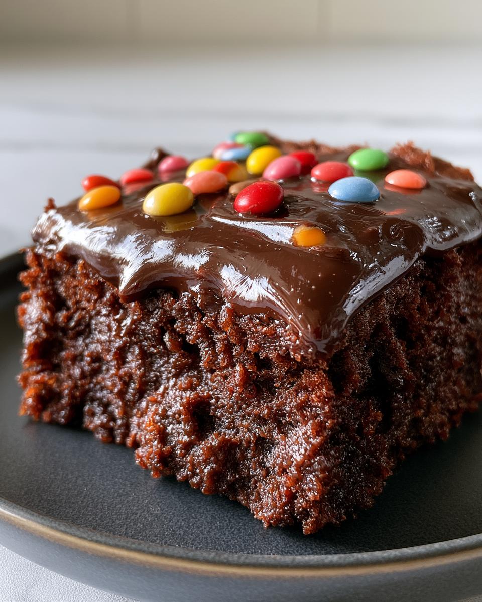Homemade Cosmic Brownies for Perfect Fudgy Texture 4 A close-up of a fudgy Homemade Cosmic Brownie topped with chocolate ganache and colorful candy-coated chocolate pieces.