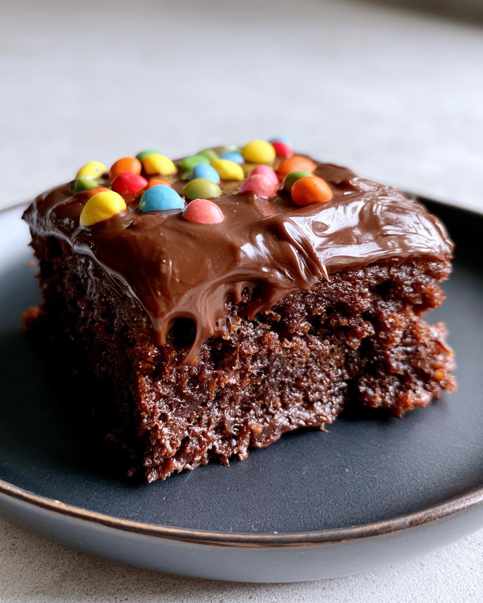 Homemade Cosmic Brownies for Perfect Fudgy Texture 5 A fudgy slice of Homemade Cosmic Brownies topped with rich chocolate frosting and colorful candy pieces.