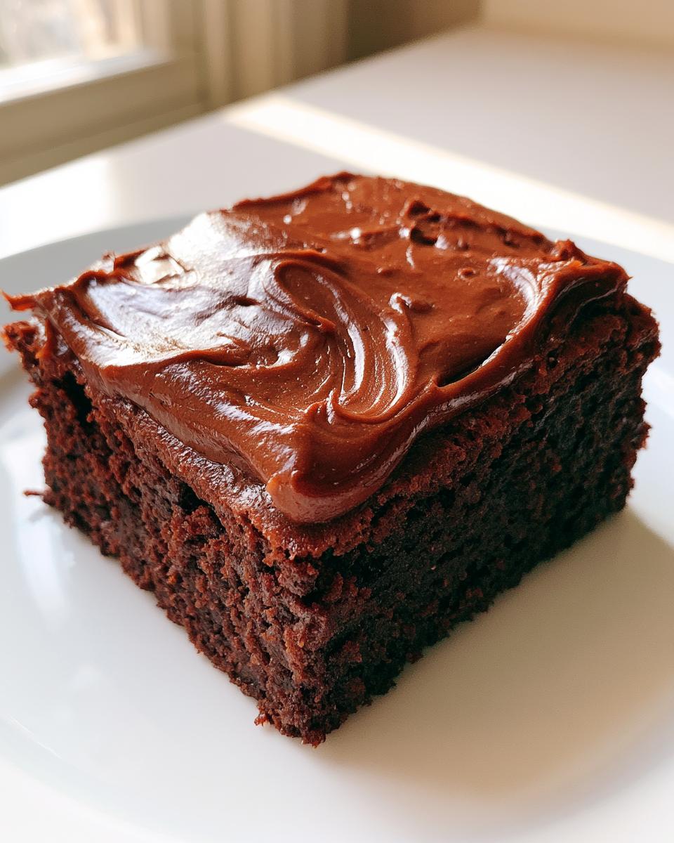 Lunch Lady Brownies: 1-Pan Fudgy Nostalgia 4 A close-up of a fudgy Lunch Lady Brownie topped with rich chocolate frosting on a white plate.